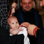 A traditional Orthodox baptism featuring a priest, baby, and family in an intimate ceremonial setting.